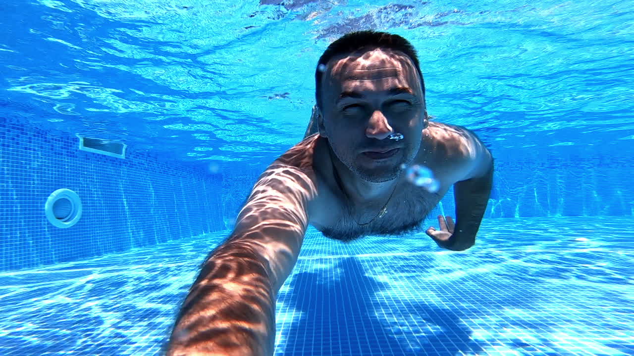 Man swimming and breathing underwater. Healthy male is diving inside the pool with underwater camera on clear blue water background.