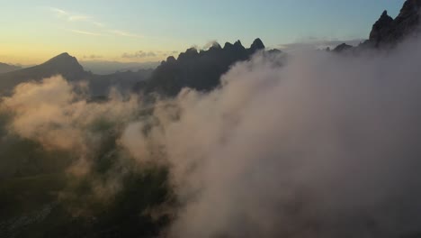 flight through clouds reveals the dolomites in italy at sunset, forward aerial