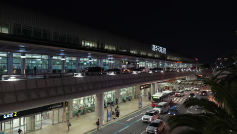 shuttle bus at the pick-up and drop-off point of jeju international airport with view of cars and passengers at night
