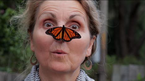 atractiva mujer de mediana edad se ve sorprendida y luego se cruza con los ojos tratando de mirar a la gran mariposa monarca descansando sobre su nariz - primer plano - 4k, 59