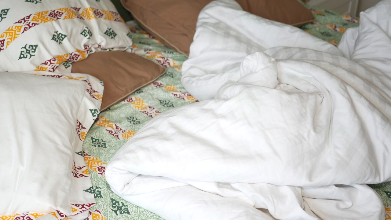 Messy Unmade Bed with White Duvet and Patterned Pillows