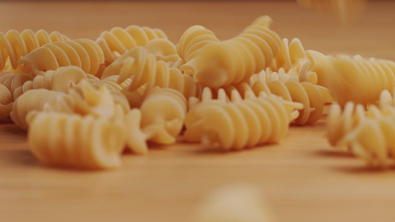 Fusilli secchi che cadono su un piano in legno al rallentatore