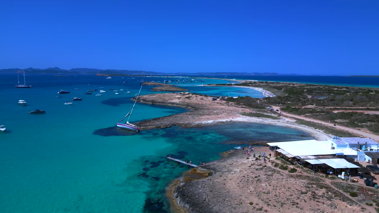 Sailboats anchored in turquoise waters near a beach Restaurant on the idyllic island Formentera, Spain. Unique aerial view flight descending drone
