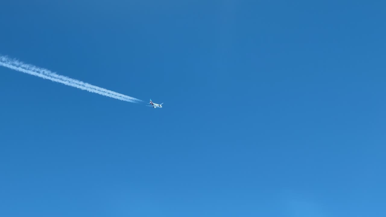 An aerial view of a twin-engine white color fuselage jet crossing diagonally a blue skt. Aerial shot taken from another jet cockpit flying bellow.