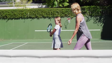 caucasian mother teaching her daughter to play tennis at tennis court on a bright sunny day