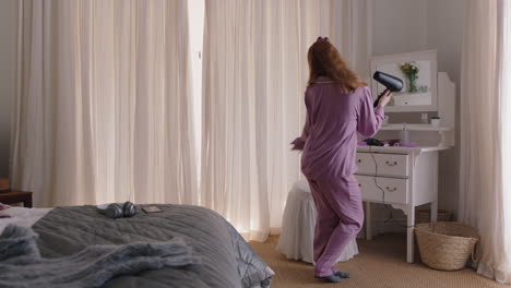 mujer divertida bailando en el dormitorio cantando karaoke con secador de pelo disfrutando de la mañana del fin de semana divirtiéndose celebrando un estilo de vida despreocupado usando pijama en casa