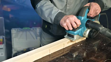 primer plano de la mano de un carpintero trabajando con un avión eléctrico en un taller doméstico