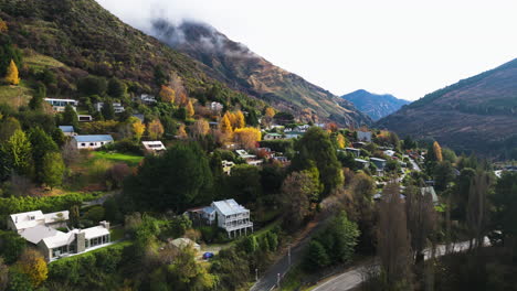 aerial drone shot over arthur's point, queenstown, new zealand with beautiful houses along mountain slope through autumn trees at daytime