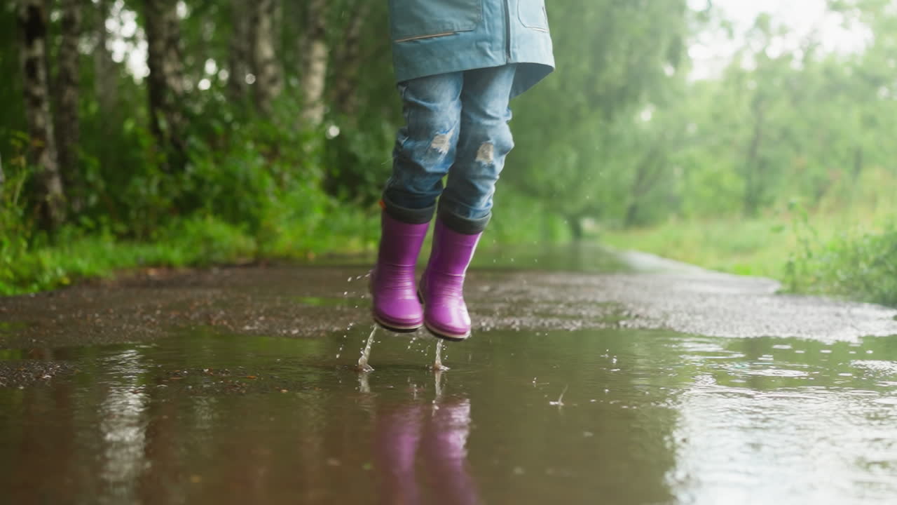 Little child jumps in puddle on park road closeup funny little boy plays splashing water water on