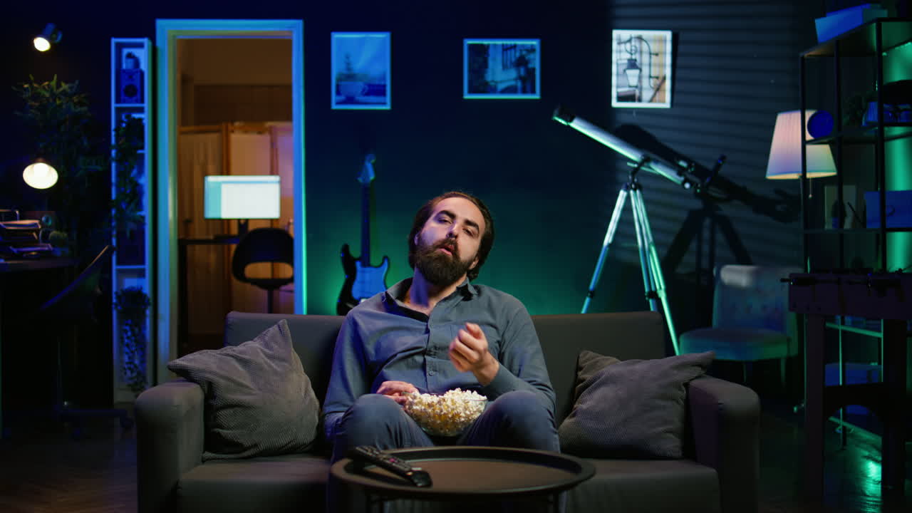 hombre fatigado viendo programas en la televisión tarde en la noche y comiendo palomitas de maíz
