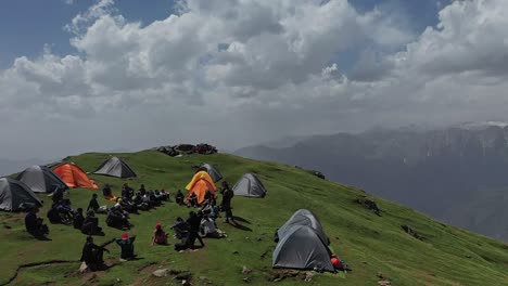 Colorful-Tents-And-Hikers-Gathered-In-Circle-Near-A-Cliffside-In-Sar-Pass-Trek---Aerial-shot