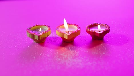 Close-up-of-burning-colourful-candles-celebrating-diwali-on-purple-background