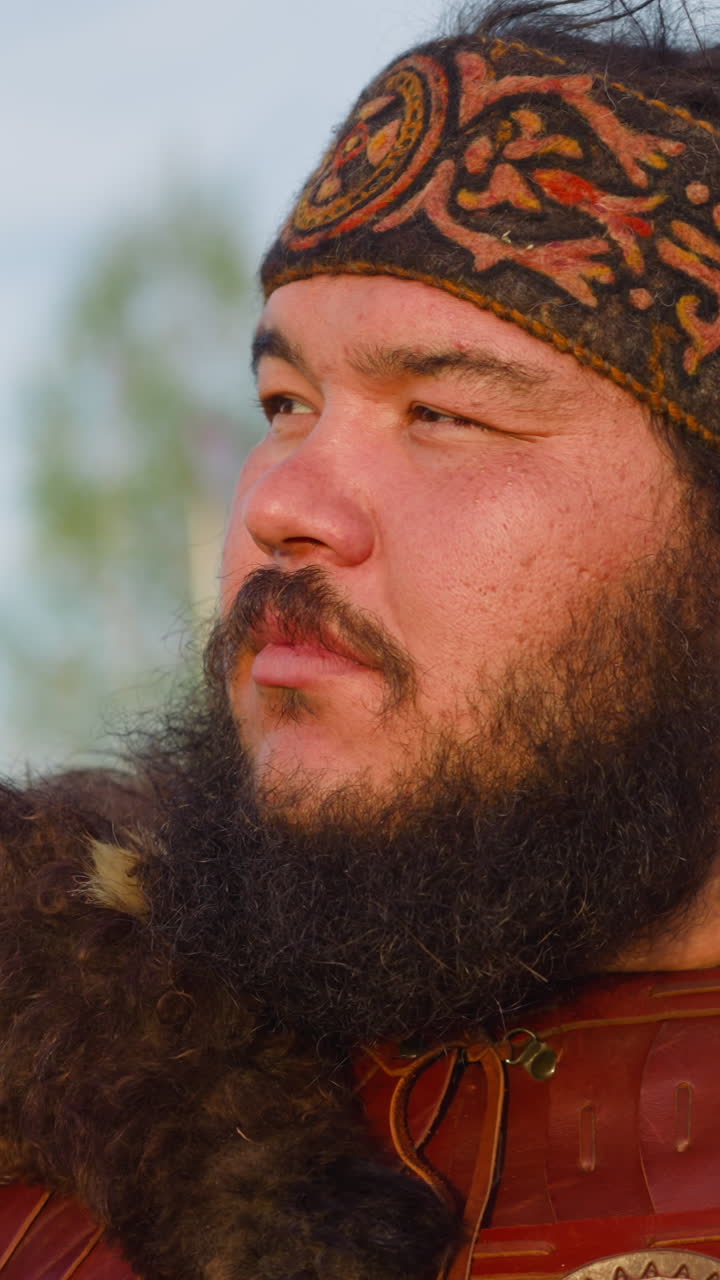 Positive man with beard and patterned headband looks in distance at highland during Altai ethnic festival closeup. Ancient culture and atmosphere