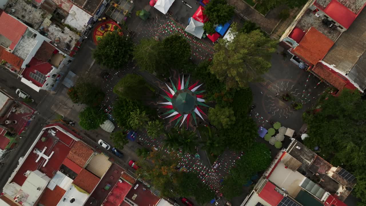 Drone top-down view over Ajijic Zócalo and park, capturing vibrant local scene in Jalisco, Mexico. Main square decorated with Mexican flag colors to celebrate the independence