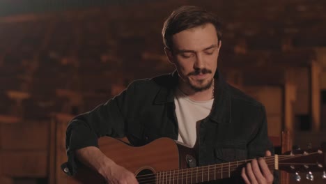 un chico guapo toca una guitarra acústica en un cine abandonado. el músico canta una canción y acompaña en la guitarra