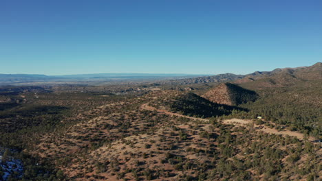 Aerial-view-of-remote-mountain-road-in-desert-with-van-camping-on-ridge,-4K