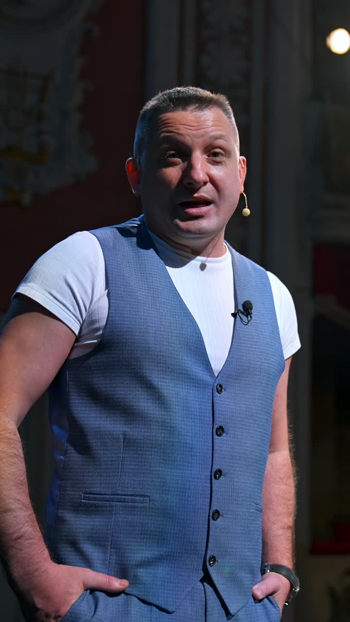 Portrait of an actor during the rehearsal. Man in grey suit standing on stage in the empty theater and talking to camera. Lockdown and world crisis. Vertical video