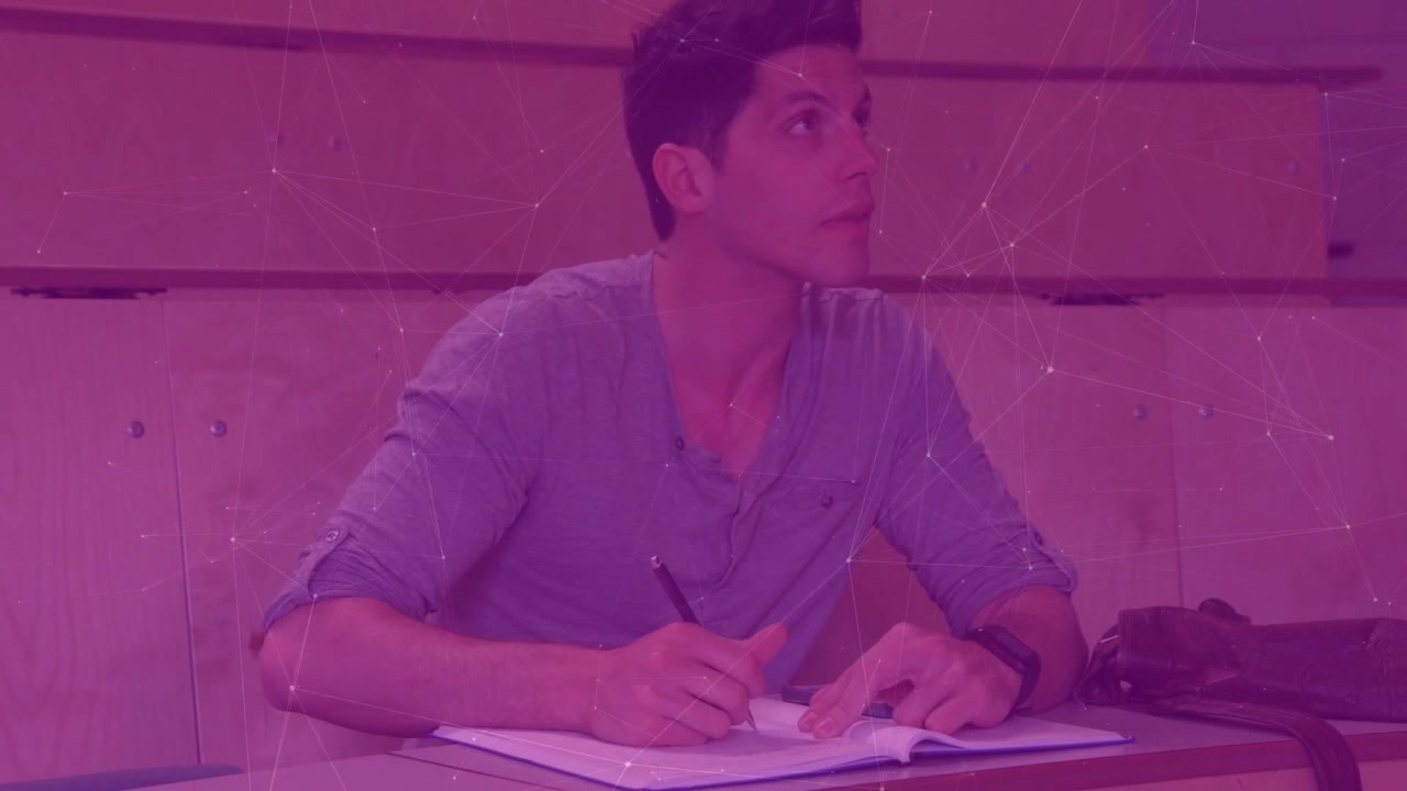 Male student placing notebook on desk, writing notes for study in lecture while glancing at speaker