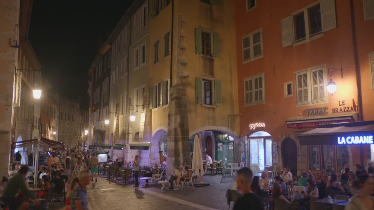 People Walking At The Old Town With Restaurants At Night In Annecy, France. - wide shot