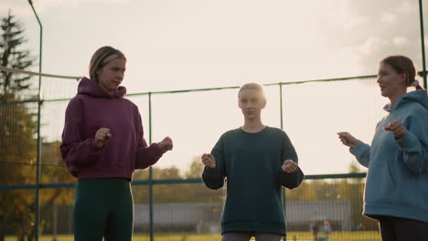 three ladies engaged in fitness activity with sunlight creating a warm glow around them, bar fence and greenery in the background, showcasing outdoor exercise in bright daylight