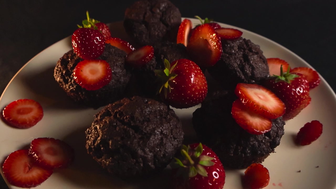 Delizioso piatto di muffin al cioccolato o brownies appena sfornati, decorati con fragole succose intere e a fette e una salsa rossa dolce, presentato su un piatto su uno sfondo scuro