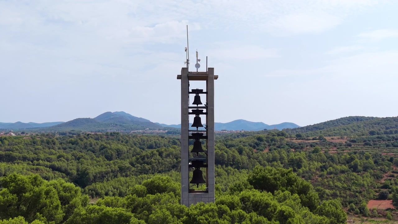 Et genanvendt minetårn, omdannet til et klokketårn, rejser sig over et grønt skovlandskab i Catalonien, Spanien, med bjerge og diset himmel i baggrunden.