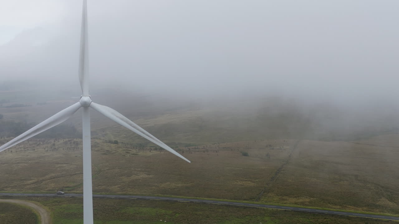 Panning drone shot of wind turbines in West Yorkshire on a grey, misty and cold morning overlooking hills and fields
