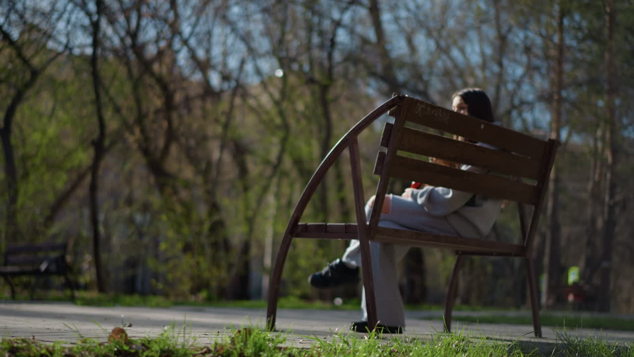 relaxed young woman on park bench, casual young lady laying under tree branches, an informal scene capturing woman in repose on park bench surrounded by bare branches during springtime