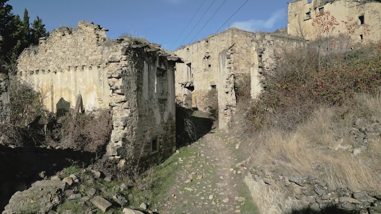 Edifici in pietra in rovina e strade invase dalla vegetazione della città fantasma abbandonata di Esco, un sito storico desolato nella regione dell'Aragona, Spagna, che mostra gli effetti del degrado e dello spopolamento