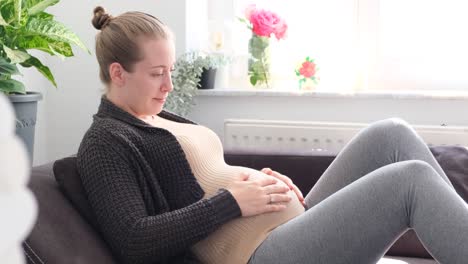 white blonde woman caressing her pregnant belly while smiling or thinking about something