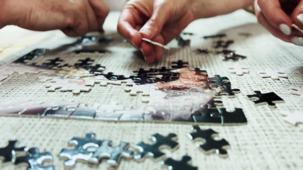 Close-up beberapa tangan berkolaborasi untuk menyusun puzzle jigsaw di atas meja. Aktivitas rekreasi kooperatif yang membutuhkan fokus dan kesabaran