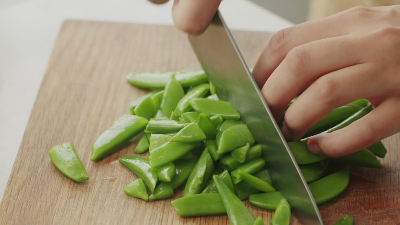 mujer cortando frijoles verdes en una tabla de madera en la cocina