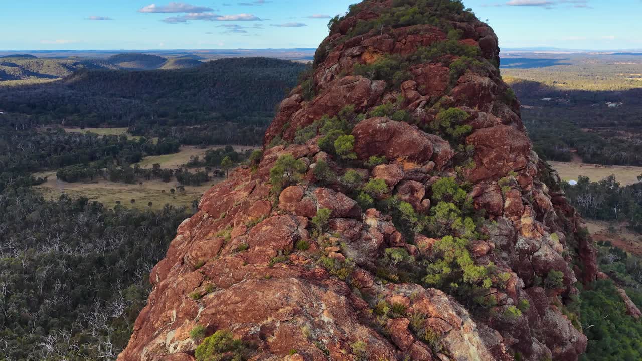 Drone glides above rugged volcanic outcrop, revealing expansive Australian landscape in warm sunset light