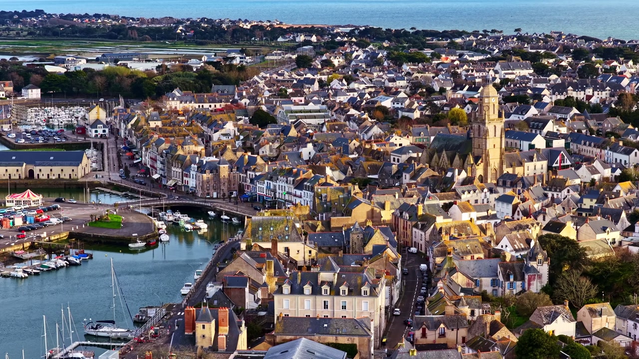 Historic harbor town with church tower marina and dense coastal buildings in Le Croisic France, aerial establishing dolly at sunset