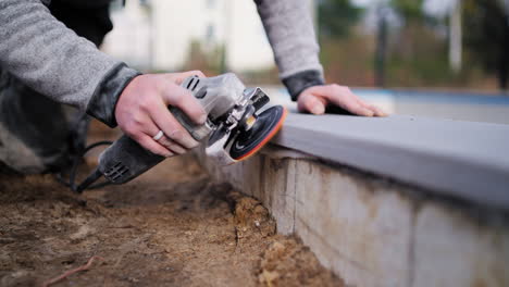 trabajador de la construcción puliendo esquinas de piso de concreto con una amoladora angular - primer plano