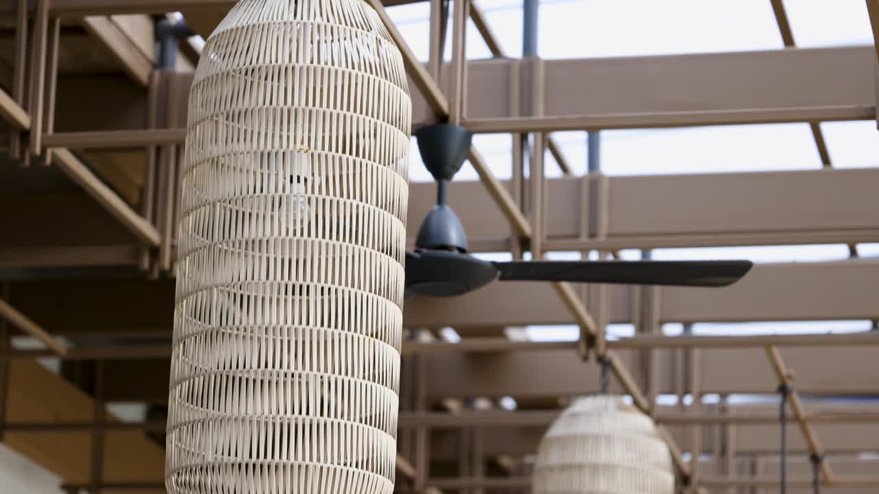 Takvifte snurrer sakte i et lyst, moderne hotellatrium med flettet innredning og naturlig belysning