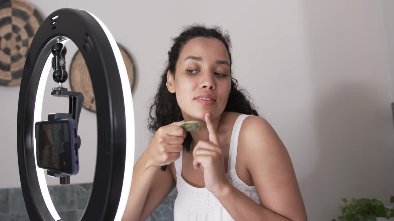 African American woman showing green guasha scraping jawline after phone prompt, filming at vanity