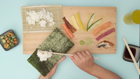 Draufsicht-Von-Zwei-Händen,-Die-Sushi-Auf-Einem-Blauen-Tisch-Zubereiten