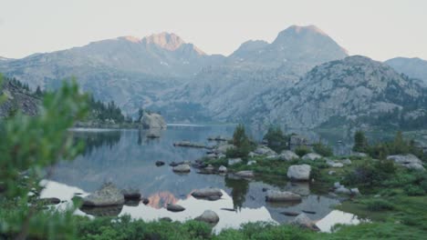 mountain lake with rocks and greenery at dawn, framed by nearby foliage