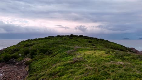 Eine-Kleine-Insel-Mit-Einem-Grasbewachsenen-Hügel-An-Der-Seite-Und-Einem-Gewässer-Im-Hintergrund