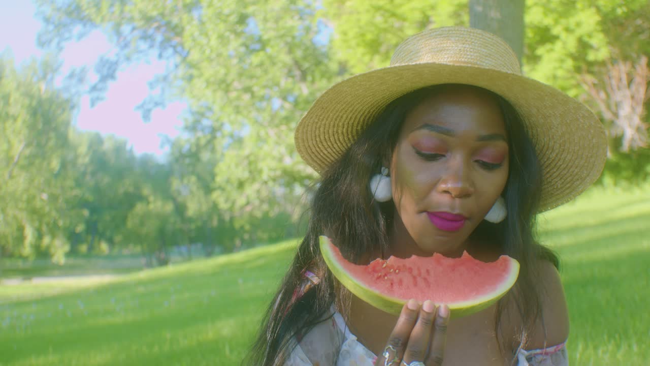 mujer negra comiendo sandía mordida disfrutando de un picnic en el parque en un día soleado