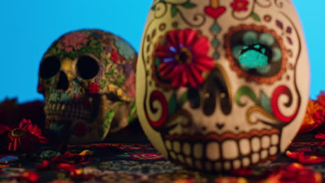 close up of decorated skulls and masks surrounded by flower petals celebrating mexican holiday of dia de muertos or day of the dead against blue background 1