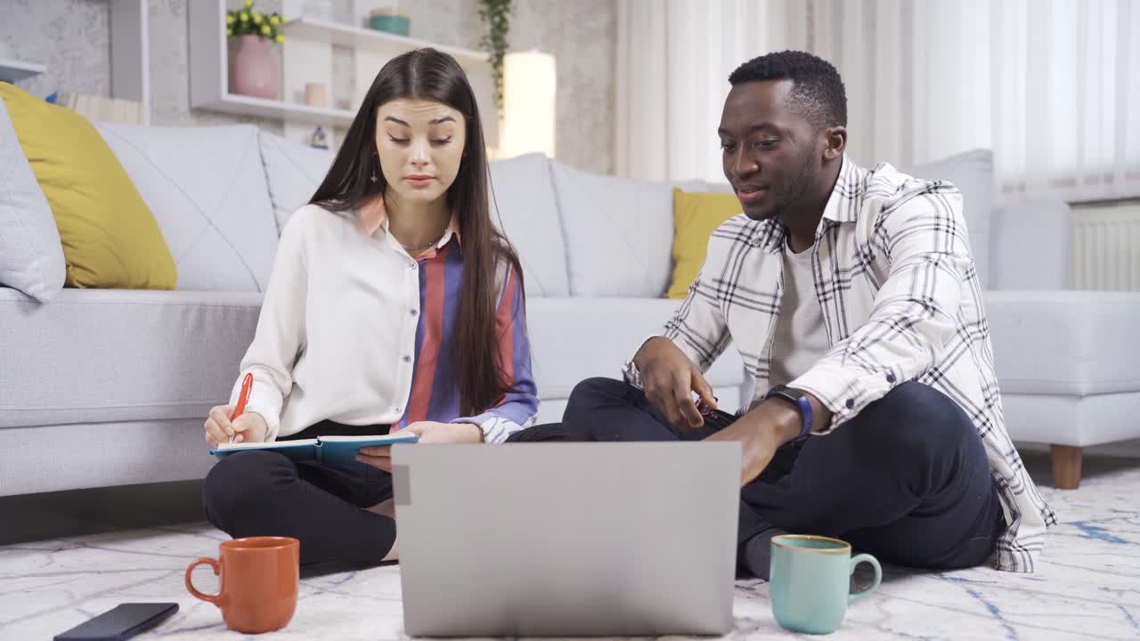 un joven estudiante universitario africano y una joven caucásica estudiando en casa, preparándose para los exámenes.