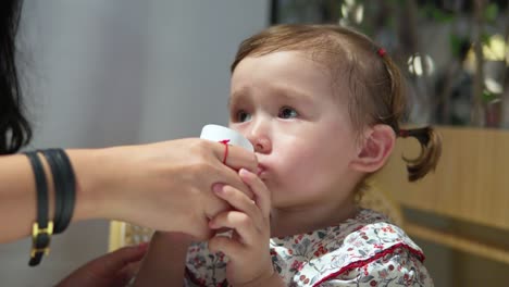 Face-close-up-of-blonde-thirsty-2-year-old-child-girl-drinking-water-from-mother's-hands-in-slow-motion