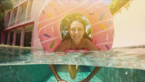 mujer con gafas de sol en bikini azul acostado en rosado inflable donut flotan en la piscina en un día soleado de verano. mira a la cámara. mujer bikini piscina en anillo de goma de sandía vacaciones relajantes