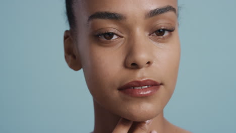 Primer-Plano-Retrato-Hermosa-Mujer-Afroamericana-Tocando-La-Cara-Con-La-Mano-Acariciando-Una-Piel-Suave-Y-Saludable-Disfrutando-De-Una-Belleza-Natural-Perfecta-Sobre-Fondo-Azul