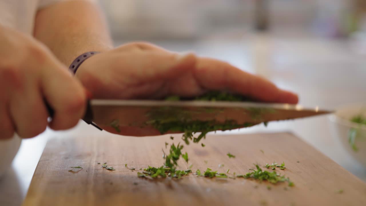 A close up clip of a male chef skilfully chopping parsley with a sharp knife on a wooden cutting board
