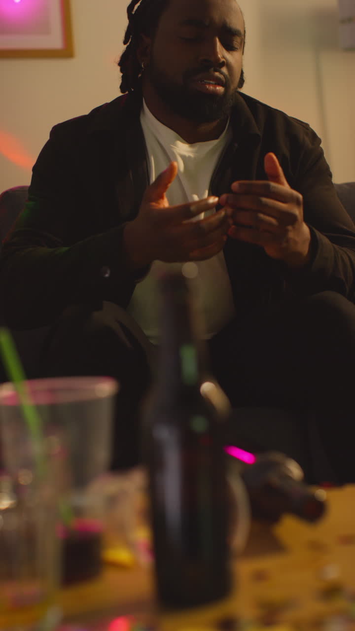 video vertical de un hombre sentado en el sofá después de beber alcohol en una fiesta en casa sufriendo de resaca