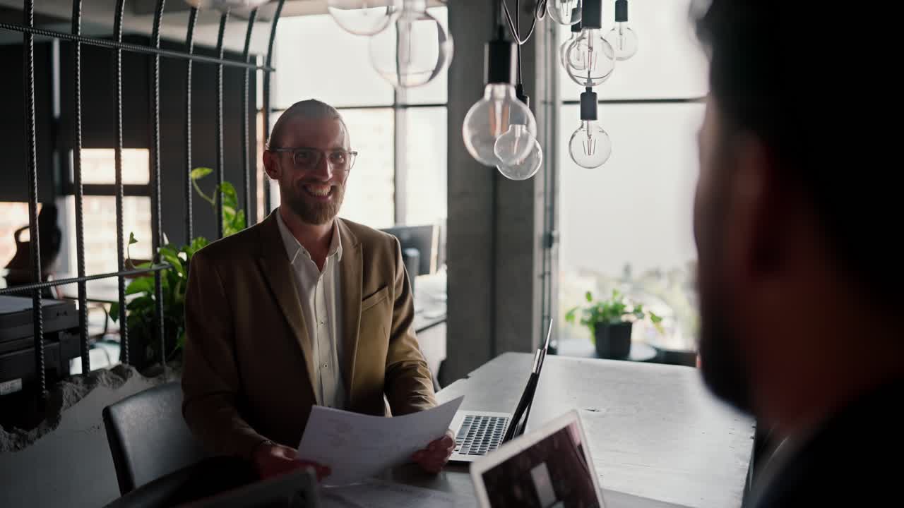 Blond man in light brown worker for an interview in a modern office. Happy blond man with a beard and glasses for an interview in a modern office