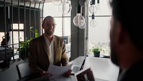 Blond-man-in-light-brown-worker-for-an-interview-in-a-modern-office.-Happy-blond-man-with-a-beard-and-glasses-for-an-interview-in-a-modern-office